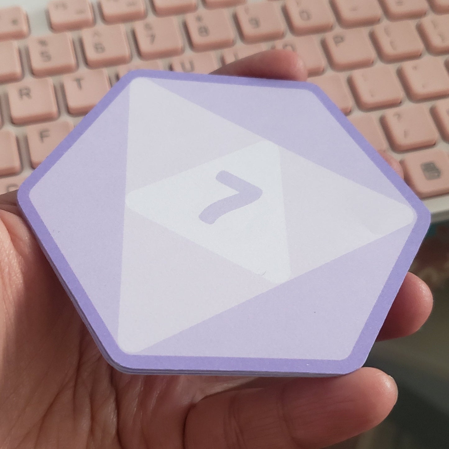 Hand holding a small purple hex shaped notepad with a d20 desing, displaying a '7' on it.