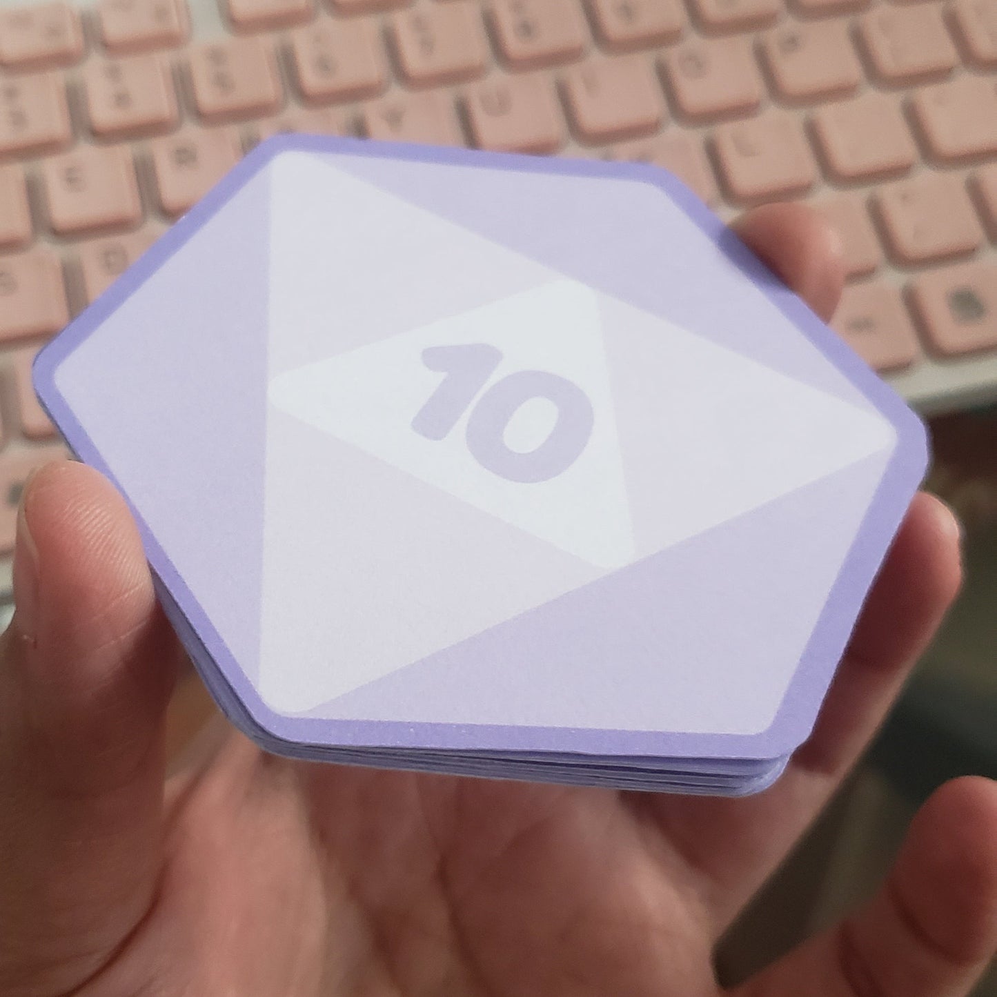 Hand holding a small purple hex shaped notepad with a d20 desing, displaying a '10' on it.